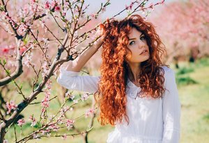 Woman with long red curly hair standing against a cherry blossom tree